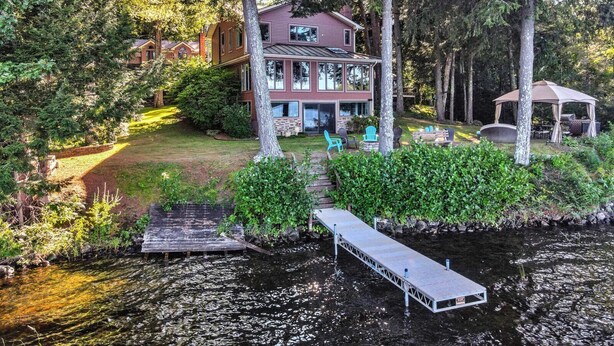 A two-story house with a dock extending into a river, surrounded by dense trees. - Spacious 5-bedroom lakefront home on pristine Lower Narrows Pond in Winthrop (Winthrop)
