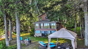 A two-story house with a glass facade, surrounded by a forested area. - Spacious 5-bedroom lakefront home on pristine Lower Narrows Pond in Winthrop (Winthrop)