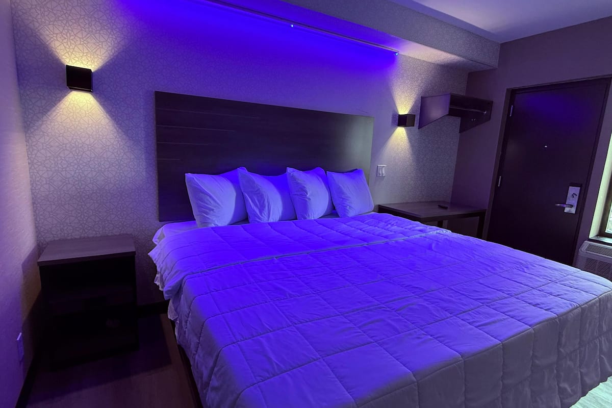 A modern hotel room with a large bed, two bedside tables, and a headboard with built-in lighting.