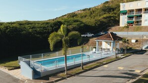A swimming pool with a fenced deck, a covered seating area, and a building with multiple balconies in the background. - Full 1st Floor Apartment with Pool - La Parguera (Lajas)