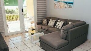 A modern living room with a sectional sofa, a glass coffee table, and a painting of a beach scene. - Full 1st Floor Apartment with Pool - La Parguera (Lajas)