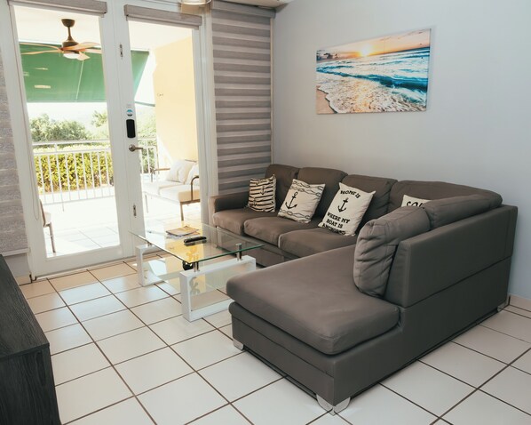 Una sala de estar moderna con un sofá seccional, una mesa de centro de vidrio y un cuadro con una escena de playa.