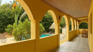 Un espacio al aire libre cubierto, con paredes amarillas, piso estampado y una piscina visible a través de un arco.