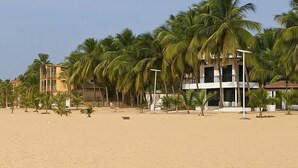 A beach with palm trees and a building with balconies.