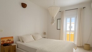Un dormitorio con cama, mesita de noche, lámpara y un cuadro en la pared.