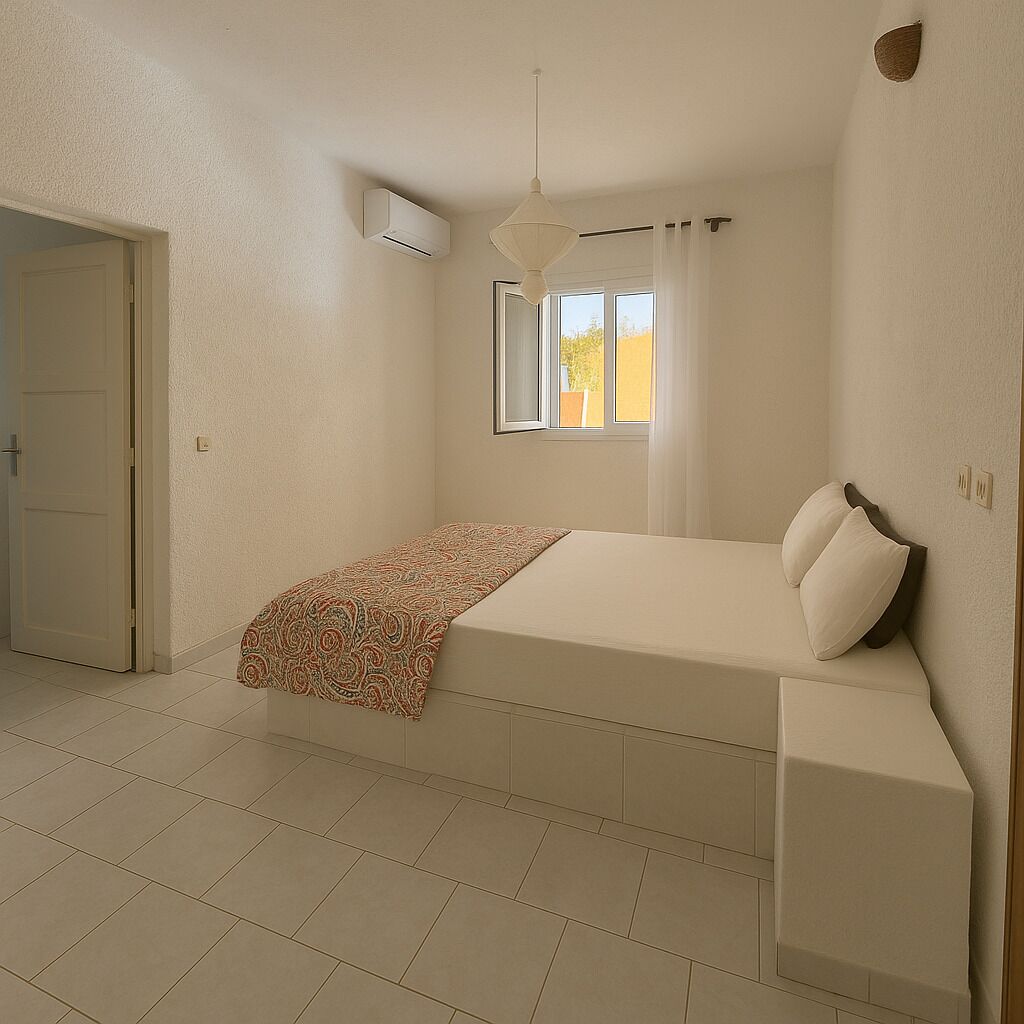 A bedroom with a bed, a window with curtains, a hanging light fixture, and a door.