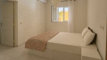 A bedroom with a bed, a window with curtains, a hanging light fixture, and a door.