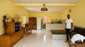 Un salón amplio con mueble de madera para entretenimiento, un comedor y una cocina al fondo.