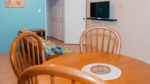 Un comedor con una mesa de madera, dos sillas, un televisor en un estante y una puerta que da a otra habitación.