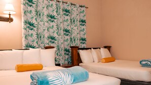 Una habitación de hotel con dos camas, cada una con ropa blanca y una sola almohada. Hay una mesita de noche de madera entre las camas y una lámpara en la pared.