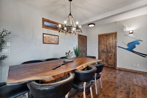 A dining area with a large wooden table, black leather chairs, a chandelier, wooden doors, and a wall-mounted light fixture.