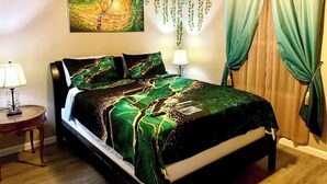 A bed with a green and black patterned bedspread, a bedside table with a lamp, and a painting on the wall. - Bohemian Home•King Bed•Long Stay•RV/Boat/Trailer Parking•RenFest (Magnolia)