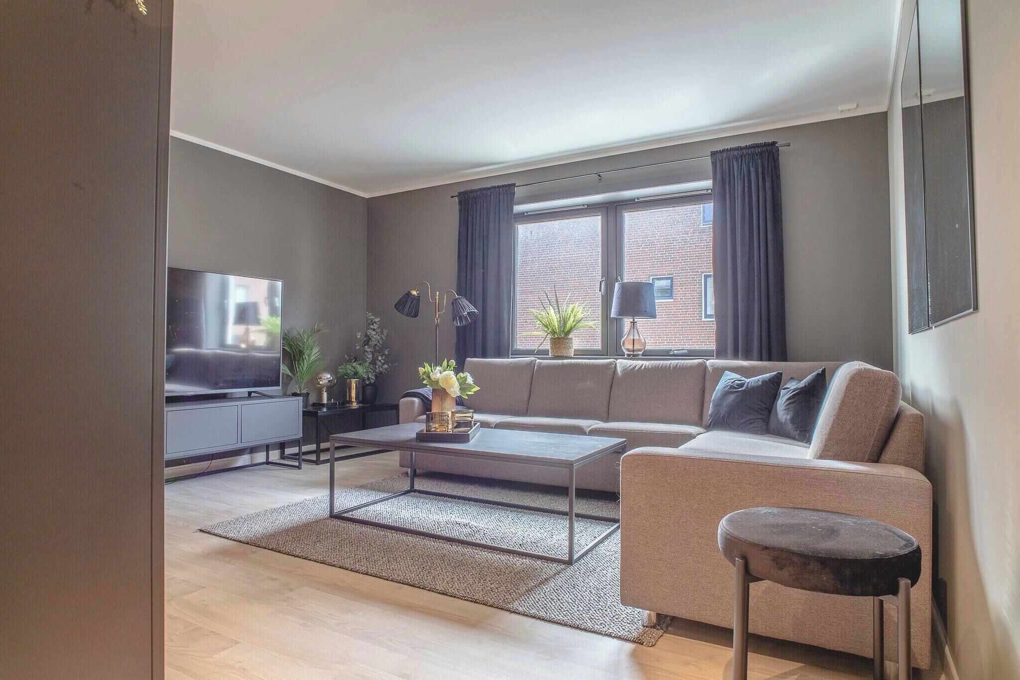 A modern living room with a sofa, coffee table, TV, and a window with curtains.