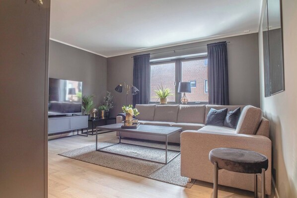 A modern living room with a sofa, coffee table, TV, and a window with curtains. - Cozy Ålesund Apartment With Private Entrance & Free Parking (Ålesund)