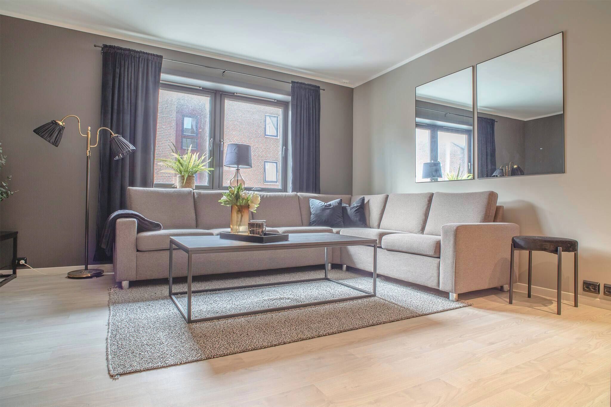 Un salon moderne avec un canapé gris, une table basse, un lampadaire et un grand miroir au mur.