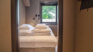 A neatly made bed with white linens in a room with a large window and a view of trees outside. - Cozy Ålesund Apartment With Private Entrance & Free Parking (Ålesund)