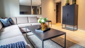 A modern living room with a sectional sofa, a coffee table with a vase of flowers, a large mirror, and a cabinet. - Cozy Ålesund Apartment With Private Entrance & Free Parking (Ålesund)