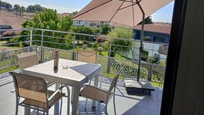 Un patio al aire libre con una mesa, sillas, un paraguas grande y vista a un barrio residencial.