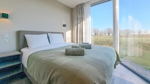 Ein Schlafzimmer mit einem großen Bett, einem Nachttisch und einem Fenster mit Blick auf ein Feld und Bäume.