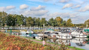 Ein Yachthafen mit verschiedenen Booten an den Liegen, umgeben von Bäumen und ruhigem Wasser.