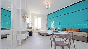 A modern hotel room with a bed, a sofa, a dining table with chairs, a mirror, and a chandelier. - Domus Augustea San Giovanni Sunset Suites (Rome)