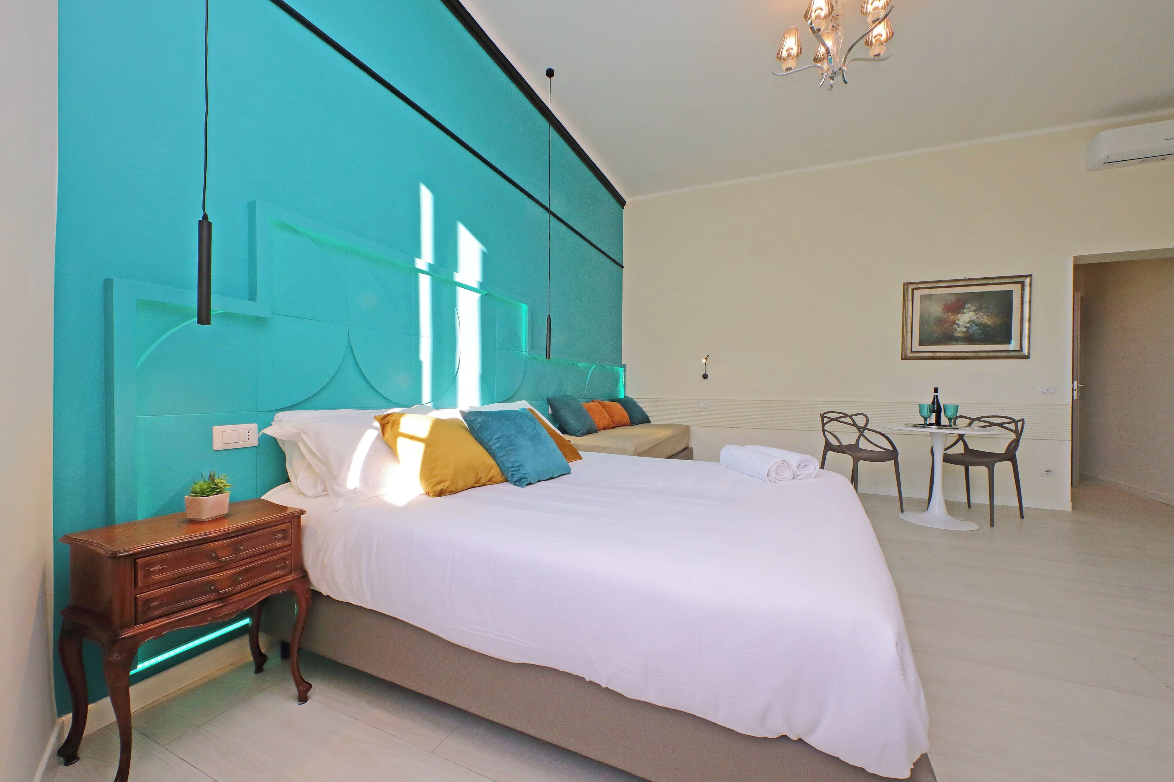 A modern bedroom with a large bed, a nightstand, a small table with chairs, and a painting on the wall.