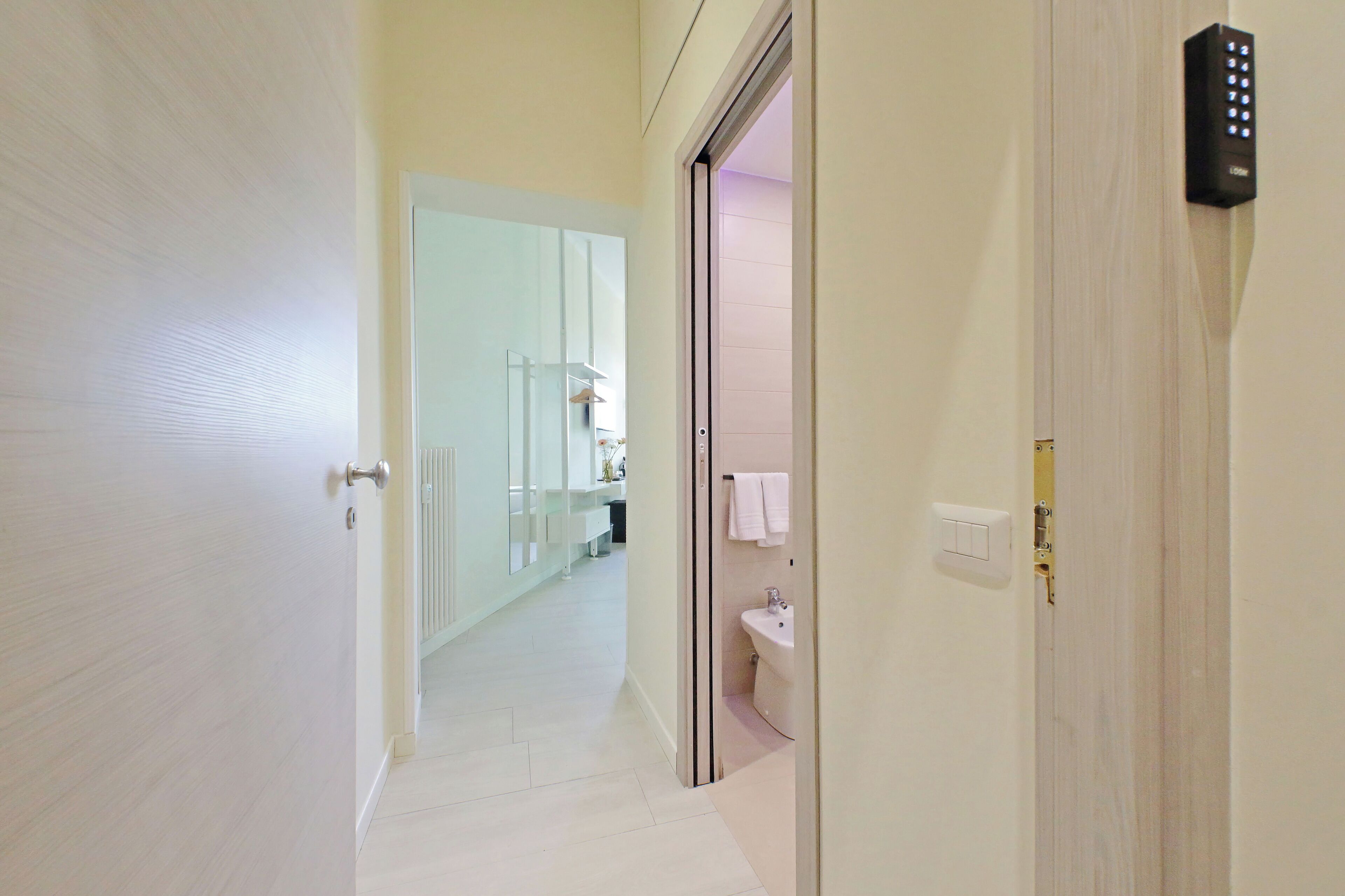 A hallway leading to a bathroom with a toilet, sink, and towel hanging on the wall.