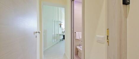 A hallway leading to a bathroom with a toilet, sink, and towel hanging on the wall.