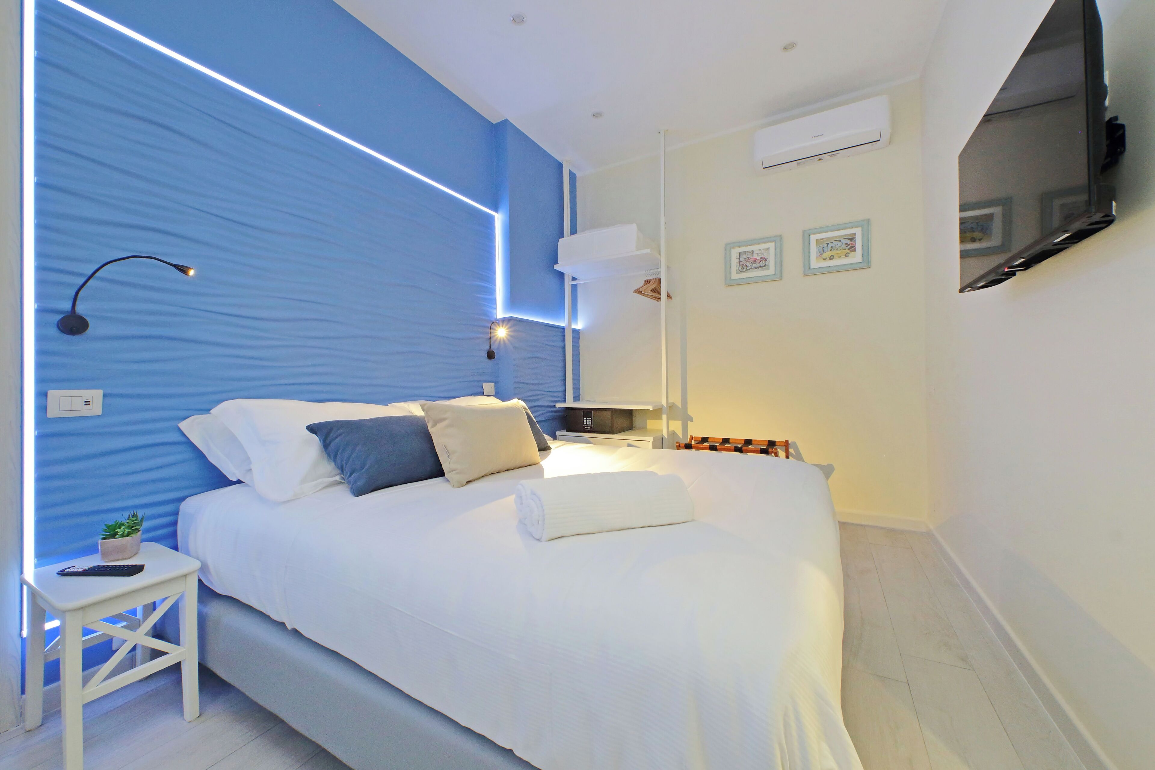 A modern bedroom with a large bed, bedside tables, a wall-mounted TV, and a blue accent wall.