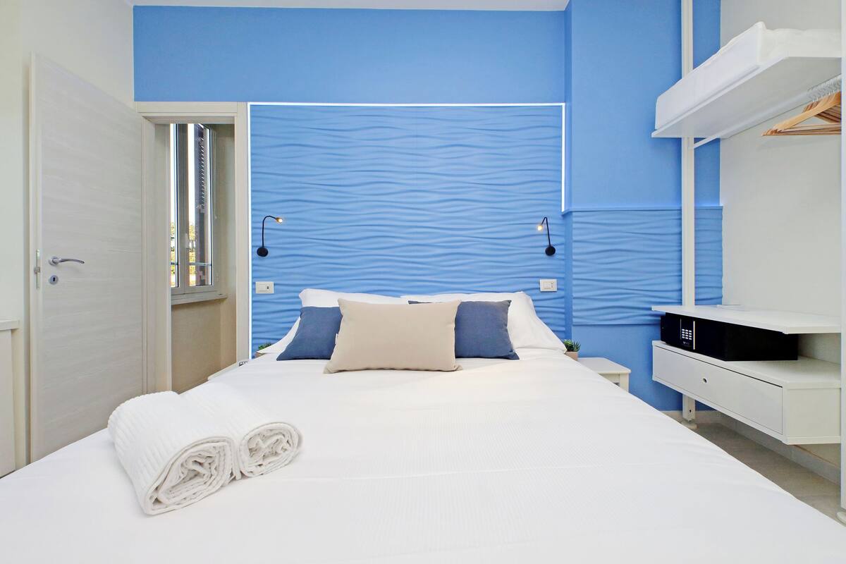 A hotel room with a bed, a nightstand, a white wardrobe, and a blue accent wall.