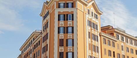 Un edificio de varios pisos con fachada amarilla, ventanas grandes y entrada en esquina.