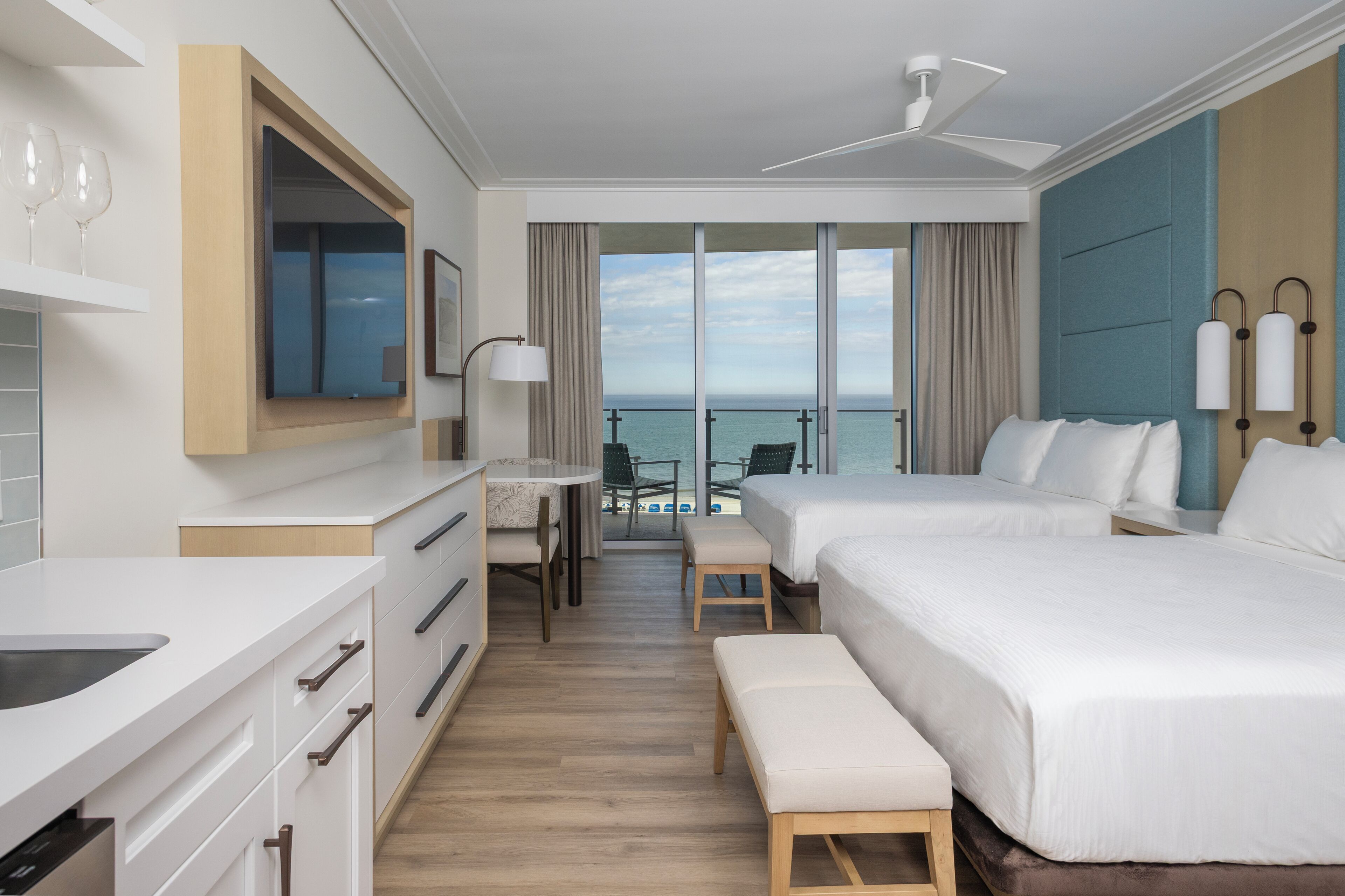 Quarto de hotel com varanda, escrivaninha, duas camas e vista para o mar.