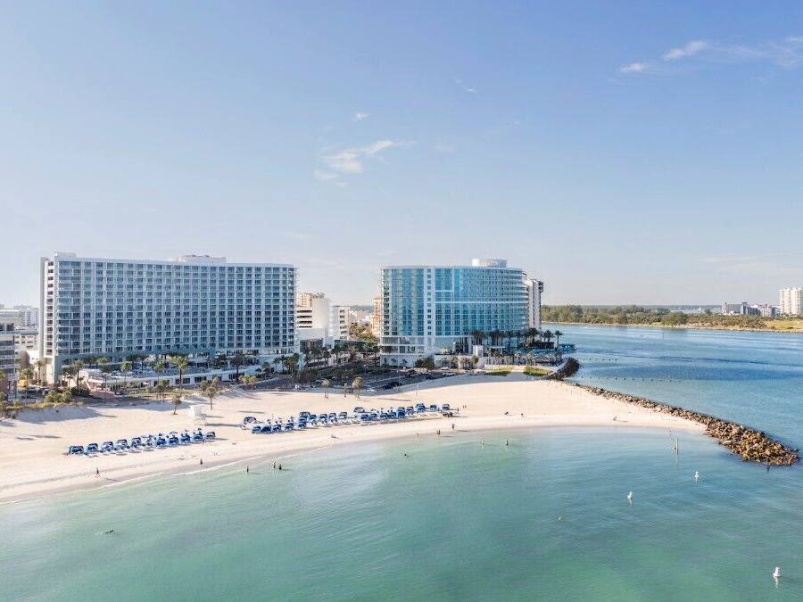 A coastal hotel with multiple high-rise buildings, a sandy beach, and a calm sea.
