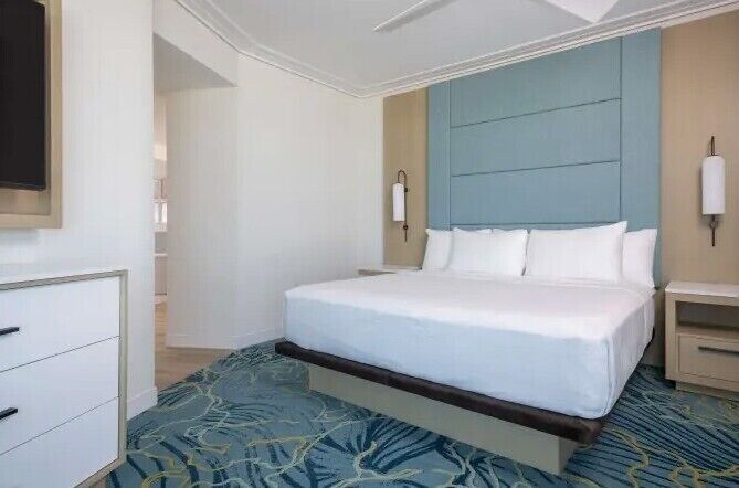Ein Hotelzimmer mit einem großen Bett, Nachttischen, einem Kleiderschrank und einem gemusterten Teppich.