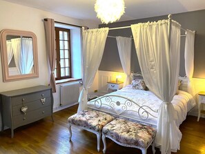 A bedroom with a four-poster bed, a nightstand, a dresser, a mirror, and a window with curtains.