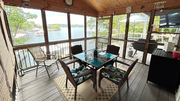 A covered outdoor seating area with a table and chairs, a clock, and a view of the lake. - Your Lake Escape Awaits! – 3BR/2BA with Private Dock in a Fun Cove at 2MM (Lake Ozark)