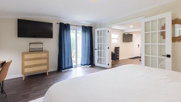 Une chambre avec un grand lit, un téléviseur fixé au mur, une commode et une porte donnant sur un balcon.