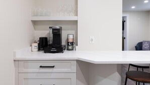 Une cuisine moderne équipée d’une machine à café Keurig, d’une cafetière et d’une pile de tasses. On peut également voir des verres à vin sur une étagère située au-dessus.