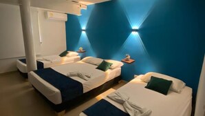 Quarto de hotel pequeno com duas camas, uma luminária no teto e um ar-condicionado fixado na parede.