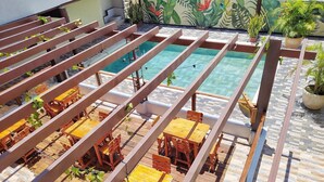Uma área de piscina com deck de madeira e mesas, cercada por plantas em vasos.