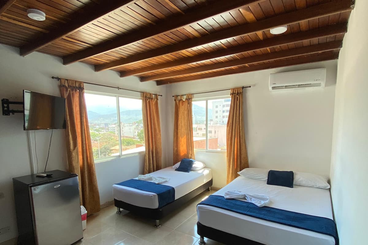 A hotel room with two beds, a TV, a refrigerator, and a window with curtains.