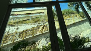 Visão pela janela de vários painéis, mostrando um edifício com varandas e um céu azul límpido.