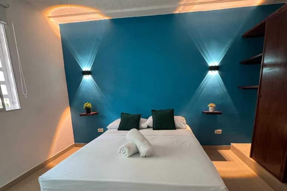 A bedroom with a bed, two bedside tables, a nightstand, a wardrobe, and a window.