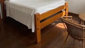 Un dormitorio con una cama de madera, una silla de mimbre, un cuadro y una ventana con cortinas.