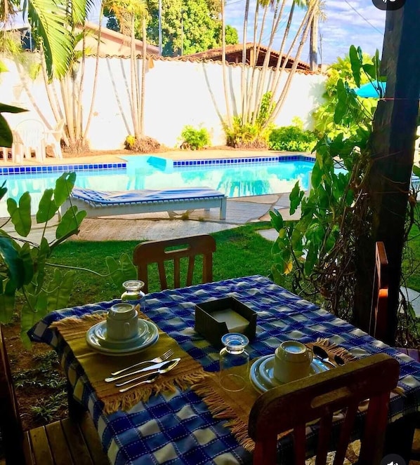 A dining table set outdoors with a view of a swimming pool. - Pousada Pouso do So Vigário (Pirenópolis)