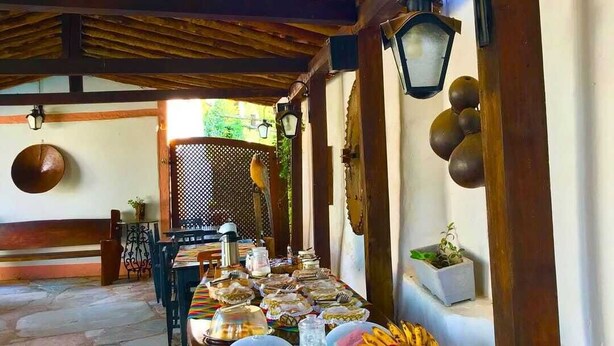 Un área de comedor al aire libre con una mesa larga preparada para una comida, rodeada de vigas de madera y faroles.
