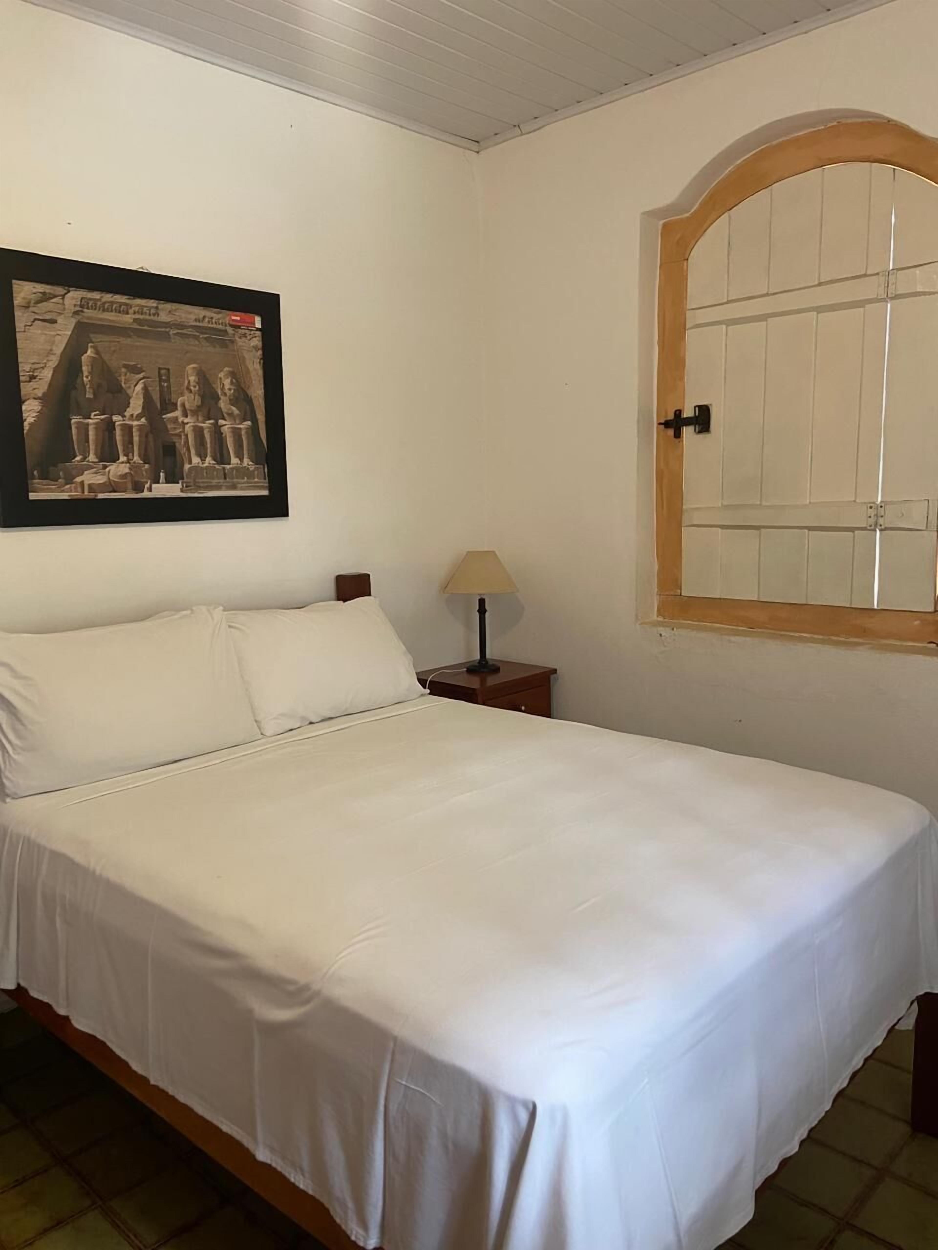 Cama bem arrumada com lençóis brancos em quarto com piso de azulejos.