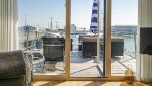 A deck with outdoor furniture, a large umbrella, and a view of the water and buildings in the background. - Nice ship in Nexø with WiFi (Nexø)
