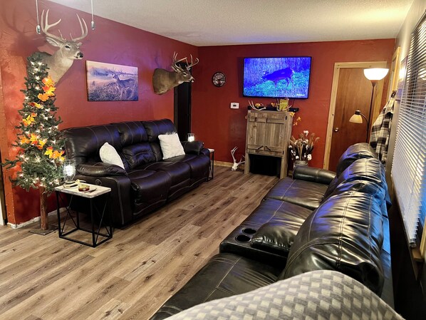 A living room with a black leather sofa, a wooden coffee table, a Christmas tree, and a mounted deer head. - Wakita Hunters Hideaway (Wakita)