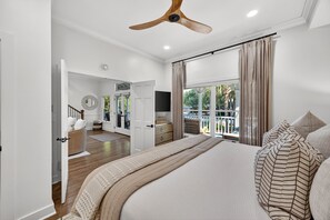 A bedroom with a large bed, a ceiling fan, a view through a window, and a door leading to another room. - 25 Atlantic Beach, Seaside Kiawah, Steps to Ocean, Pool Access! (Kiawah Island)